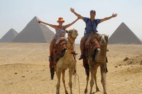 Giro del cammello al tramonto vicino all'altopiano delle piramidi di Giza